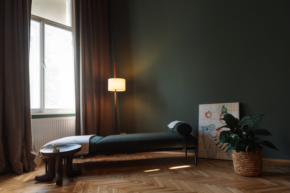 Liegebereich der Praxis: dunkelgrüne Analyseliege am Fenster, Fischgrätparkett, warmes Licht einer Stehlampe